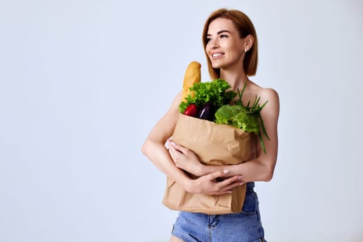 beautiful slim woman holding paper bag with vegetables on gray background. healthy food. copy space. Diet concept