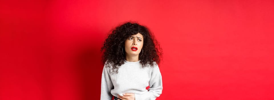 Woman feeling sick, bending and touching belly, having stomach ache or menstrual cramps, standing on red background