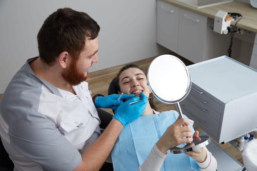 Young Woman checking her beautiful smile in mirror after stomatological treatment