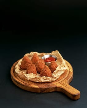 Deep fried crispy Camembert with cranberry sauce in a decorative pan on wooden background. Close up, selecive focus