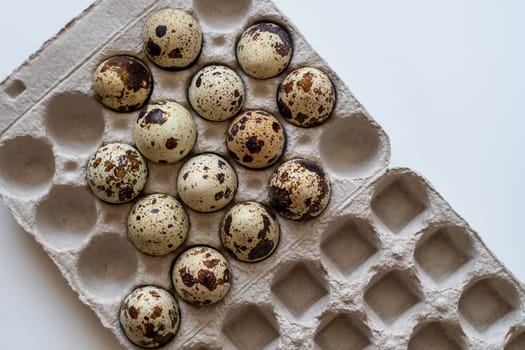 Spotted quail eggs in an egg box on a light background, natural eco-friendly products.