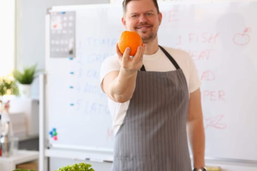 Male blogger cook holding orange and giving training lesson on how to cook healthy food