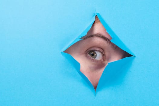Woman peeking out of hole in blue paper background.