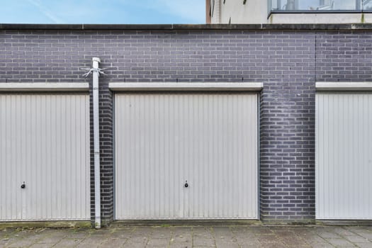 two garage doors on the side of a brick building with blue sky and white clouds in the door is closed