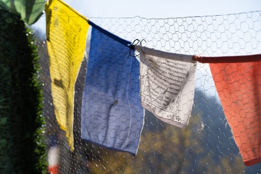 sacred religious multicolored prayer flags on fence moving in the wind showing a bhuddist prayer incantation common in hill stations in Himachal Pradesh