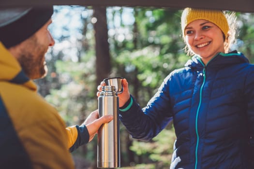 Smiling caucasian woman giving cheers with tea cup, before starting a hike with her partner