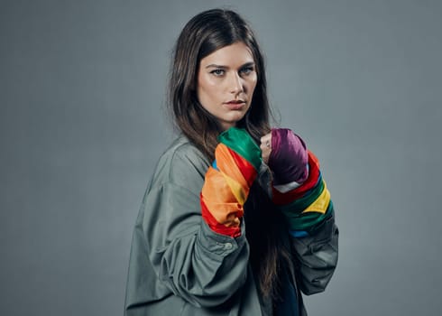Woman, fists and pride colors in protest for gay, LGBTQ or human rights against gray studio background. Portrait of female activist standing ready in fighting pose for equality or sexuality on mockup