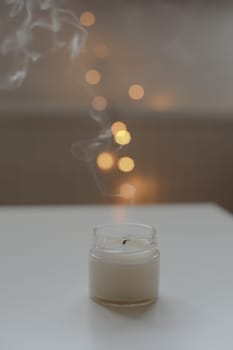 Cozy home interior decor, burning candle on table against blurred lights. Handmade scented soy wax candle in a glass. space for text.