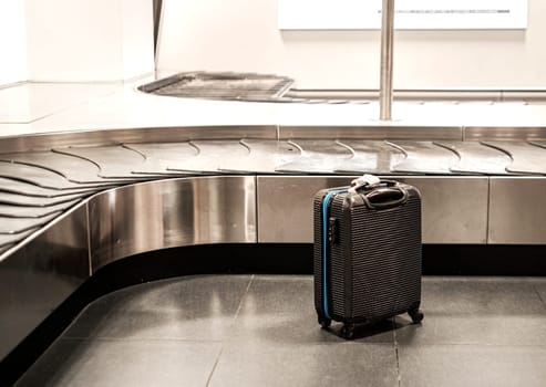 Black suitcase next to the baggage conveyor belt at the airport