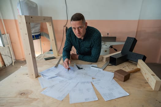Portrait of a carpenter in a plaid shirt draws a workshop blueprint.