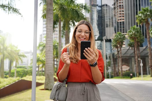 Young businesswoman using phone when walking outside office
