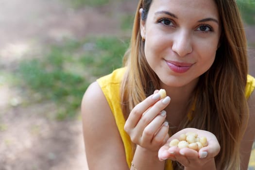 Healthy girl picking macadamia nuts from her hand in the park. Looks at camera.