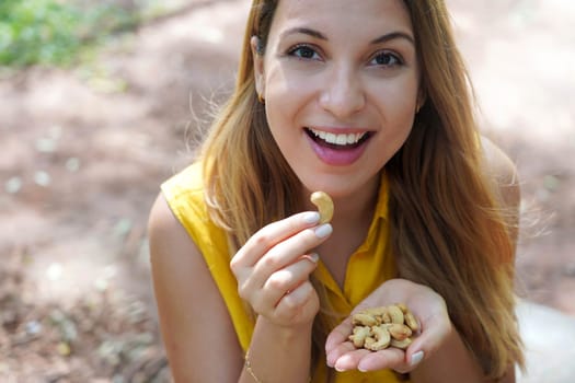 Beautiful healthy girl eating cashew nuts in the park. Looks st camera.