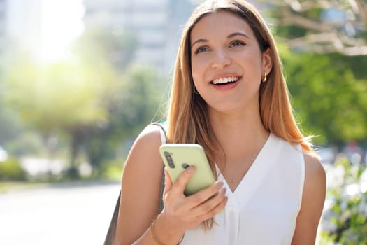 Close-up of laughing casual woman looking away holding her mobile phone outdoors 