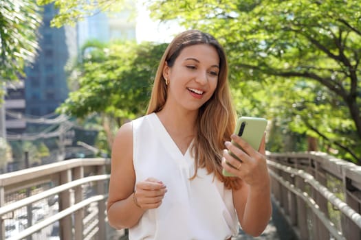 Young Brazilian businesswoman in modern natural city watching her smartphone