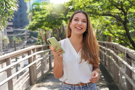 Attractive Brazilian female entrepreneur walking in Sao Paulo sustainable metropolis holding a smartphone