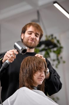 man hairdresser dries female hair with hairdryer after washing