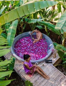 Couple relaxing in a bathtub in the rainforest of Thailand during vacation with flowers in the bath