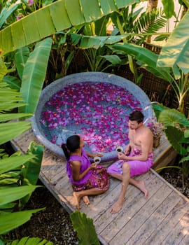 Couple relaxing in a bathtub in the rainforest of Thailand during vacation with flowers in the bath