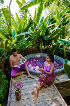 Couple at a bathtub in the rainforest of Thailand during vacation with flowers in the bath