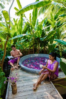 Couple at a bathtub in nature of Thailand during vacation with flowers in the bath drinking coffee