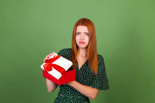 Young red hair woman on green background with gift box unhappy sad disappointed