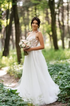 portrait of an elegant bride girl on a path in a deciduous forest with a bouquet