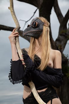 Woman in crow mask with bare breasts and old tree.
