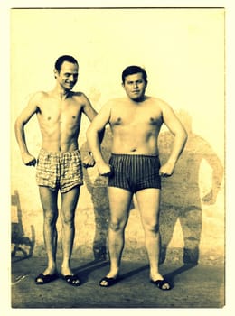 A vintage photo shows men and their muscular bodies. Photo has sepia effect.