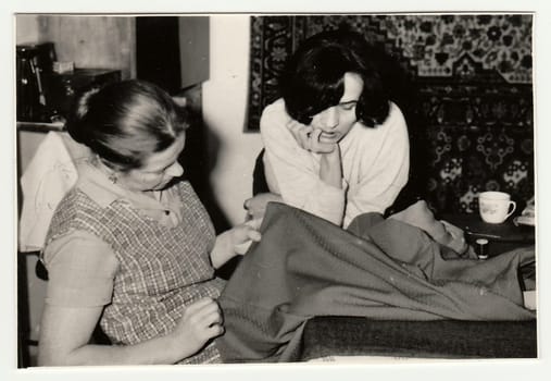 Vintage photo shows women prepare to sew a dress.