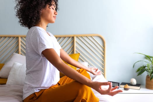 Woman meditating and breathing yoga exercises to calm mind. African American woman does meditation in bedroom.