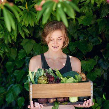 Let food be thy medicine and medicine be thy food. A young woman holding a crate of vegetables outdoors.