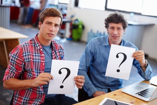 Theyre a little confused...Portrait of two coworkers looking confused while holding question mark signs.