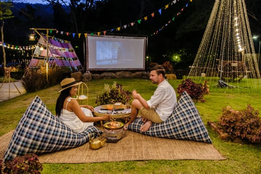 Couple watching a movie at an outdoor cinema film in a tropical garden with christmas lights