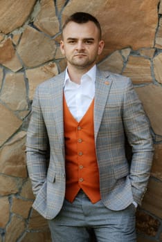 portrait of the groom in a gray suit and an orange vest