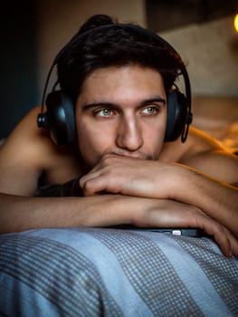 Young Man Using Headphones Lying Alone On His Bed
