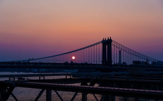 Rising sun through the ropes of the Manhattan bridge at dusk