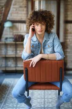 Smiling woman in denim jacket and jeans sitting on chair