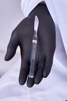 Hand in a surgical glove holding a scalpel.