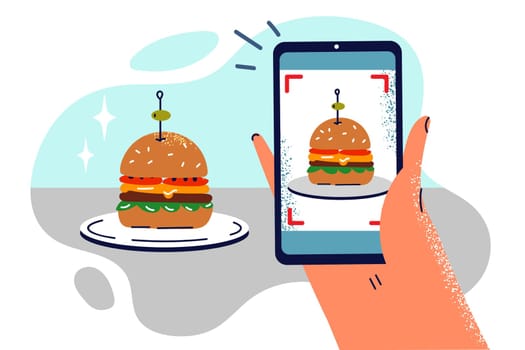 Hand with phone taking photo of hamburger on plate to share snapshot of lunch on social networks