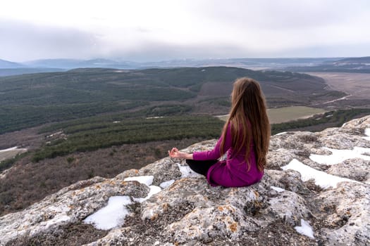 A beautiful woman sits in a lotus position on a high place with an amazing view of the mountains and the gorge practicing yoga meditation Kundalini energy thinking intuition prana. Loneliness harmony mental freedom concept