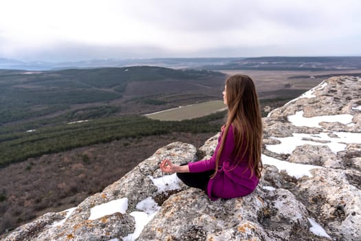 A beautiful woman sits in a lotus position on a high place with an amazing view of the mountains and the gorge practicing yoga meditation Kundalini energy thinking intuition prana. Loneliness harmony mental freedom concept
