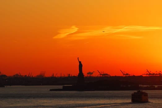 Silhouette of Statue of Liberty and Liberty Island in New York against an orange sunset sky