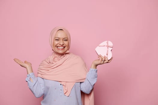 Pretty woman in pink hijab, expressing amazement and happiness while getting happy present for birthday or festive event