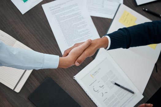 Business, hands and handshake with documents above paperwork for employment agreement or analysis at the office. Hand of people in partnership shaking for corporate contract, welcome or b2b meeting