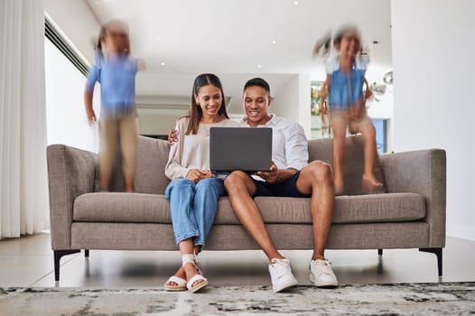 Busy, children and parents streaming a movie on the internet with a laptop on the living room sofa in house. Man and woman with a show on a computer while kids play and jump with energy on the couch