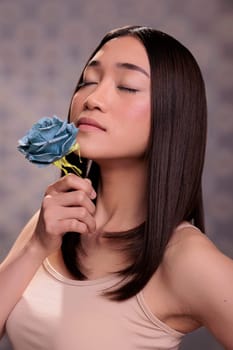 Asian woman with closed eyes enjoying blue rose smell