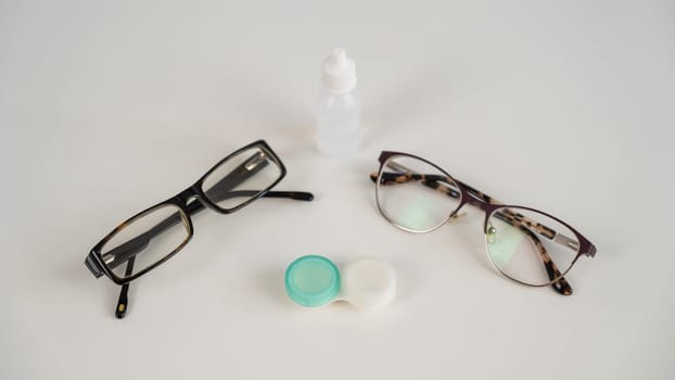Two pairs of glasses lenses and contact drops in the eyes on a white table.