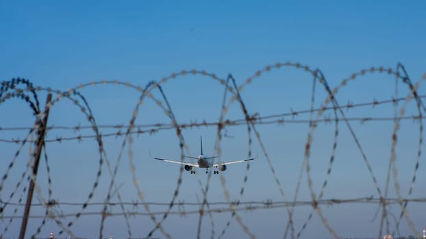 View through the barbed wire of a landing plane against the blue sky.