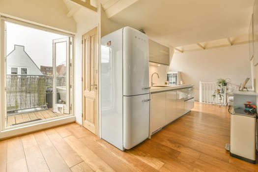 Amsterdam, Netherlands - 10 April, 2021: a kitchen with wood flooring and white refrigerator freezer in the door is open to an outdoor patio area